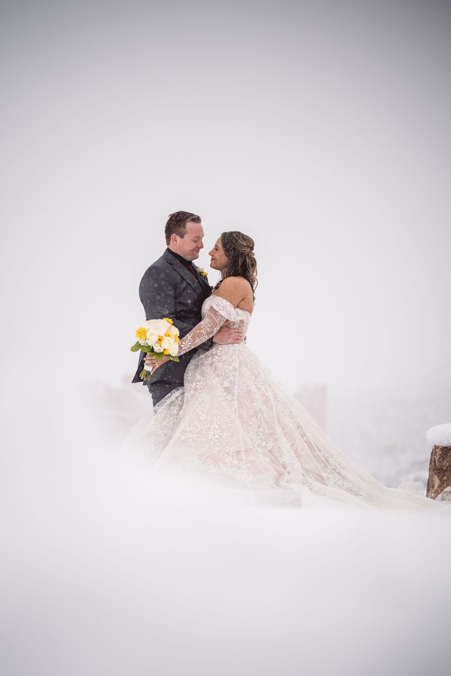 Bride and groom embrace in a snowy winter wonderland wedding portrait with yellow bouquet.