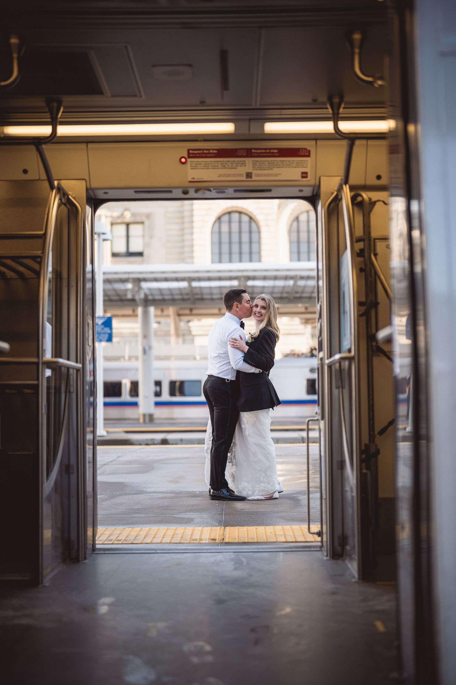 Bride and groom share a romantic kiss framed in train doors at a city station.