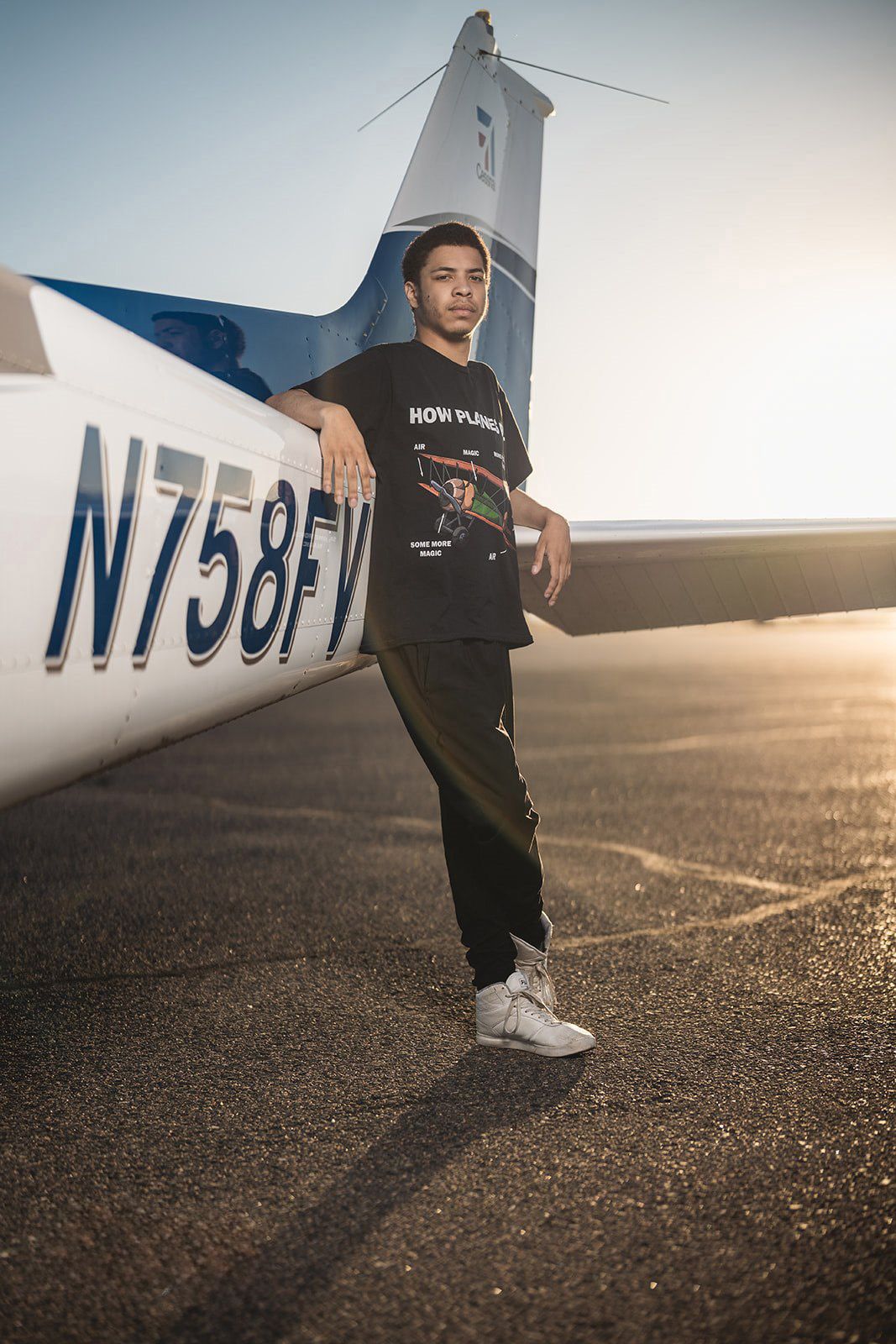 Person in black outfit posing next to a white aircraft tail number on an airfield.
