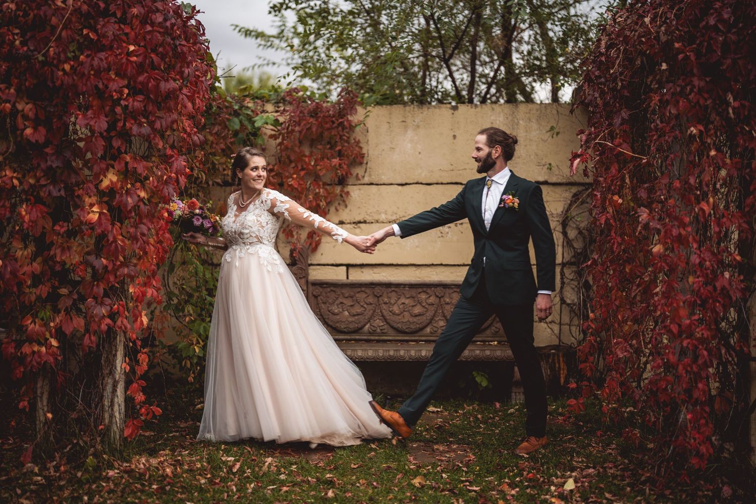 Whimsical wedding pose with couple holding hands between autumn vine archways.