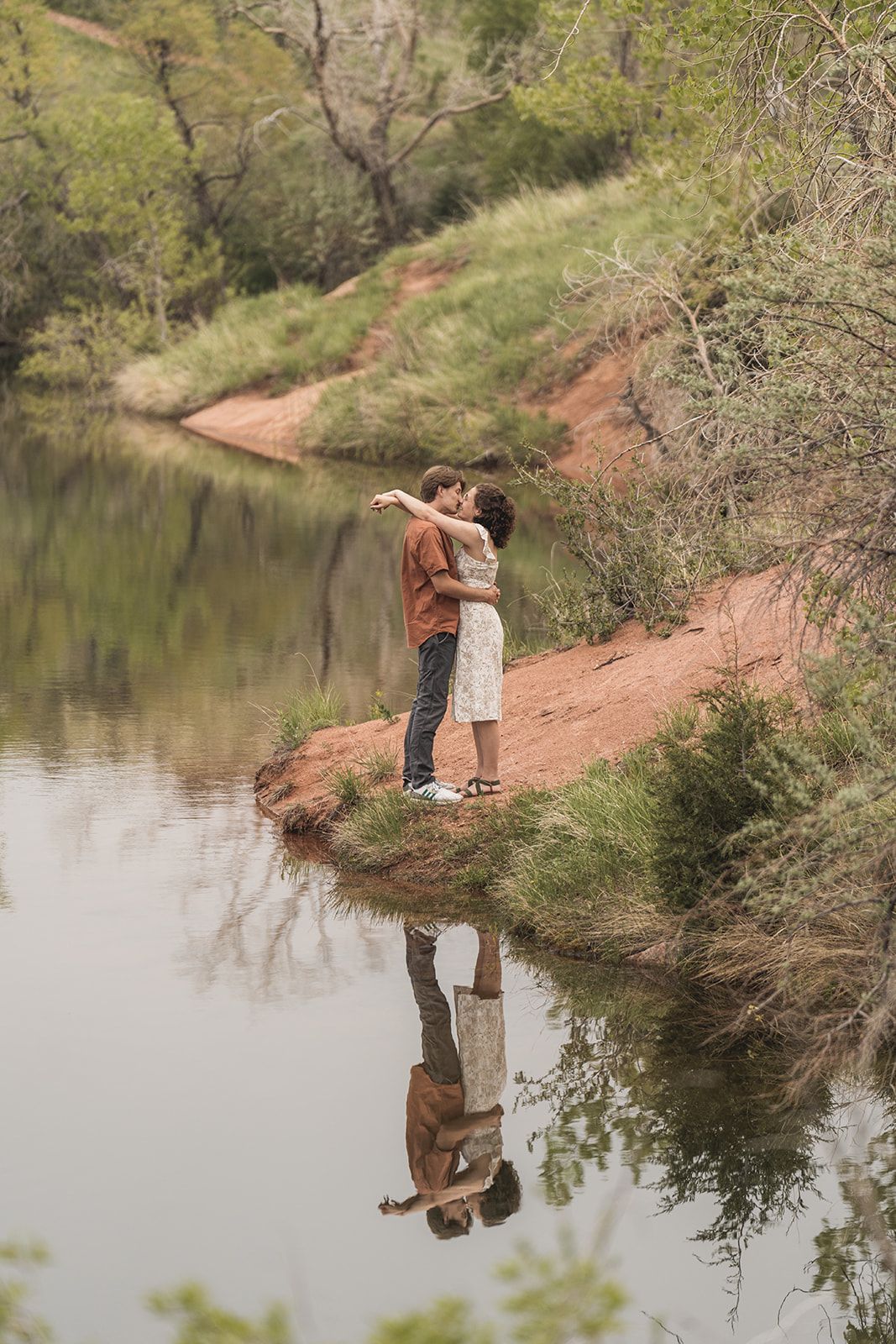 Romantic moments captured along a serene lakeside with red clay banks.