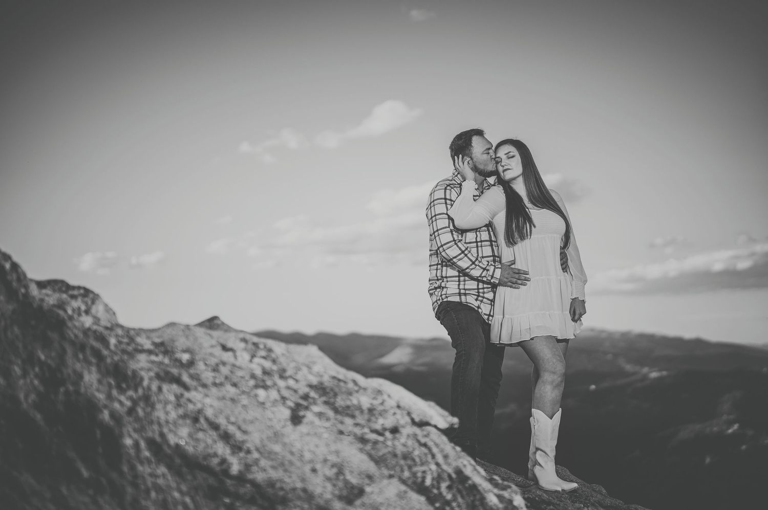 Silhouetted figures stand on mountain peak during dramatic sunset engagement photoshoot.