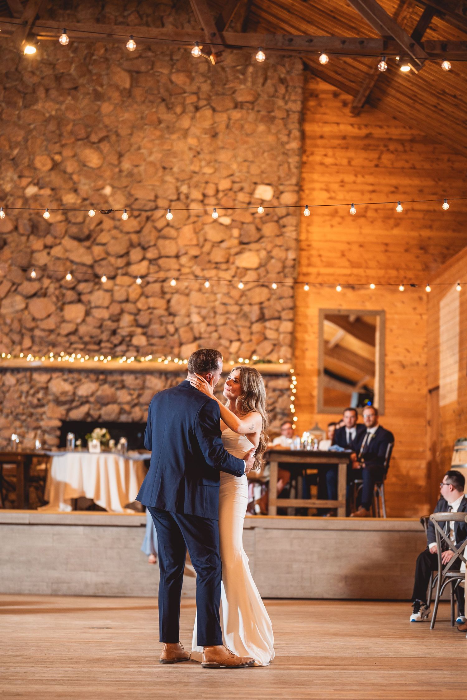 Couple dancing in a rustic venue with stone walls and string lights.
