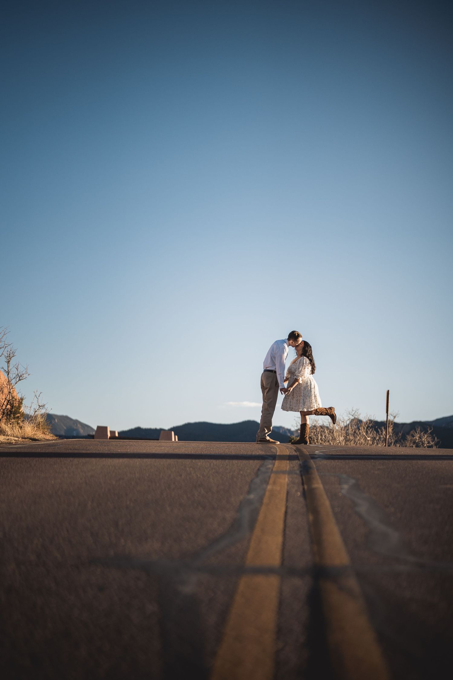 A couple creates long shadows on a desert road during golden hour.