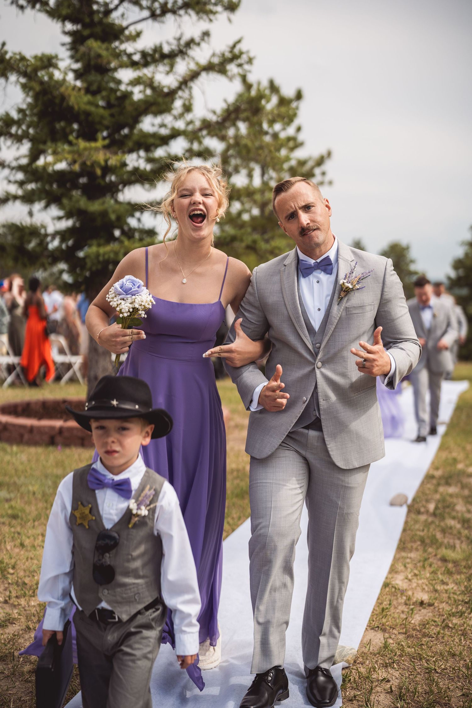 Wedding party members walking and laughing together outdoors on a grassy hill.
