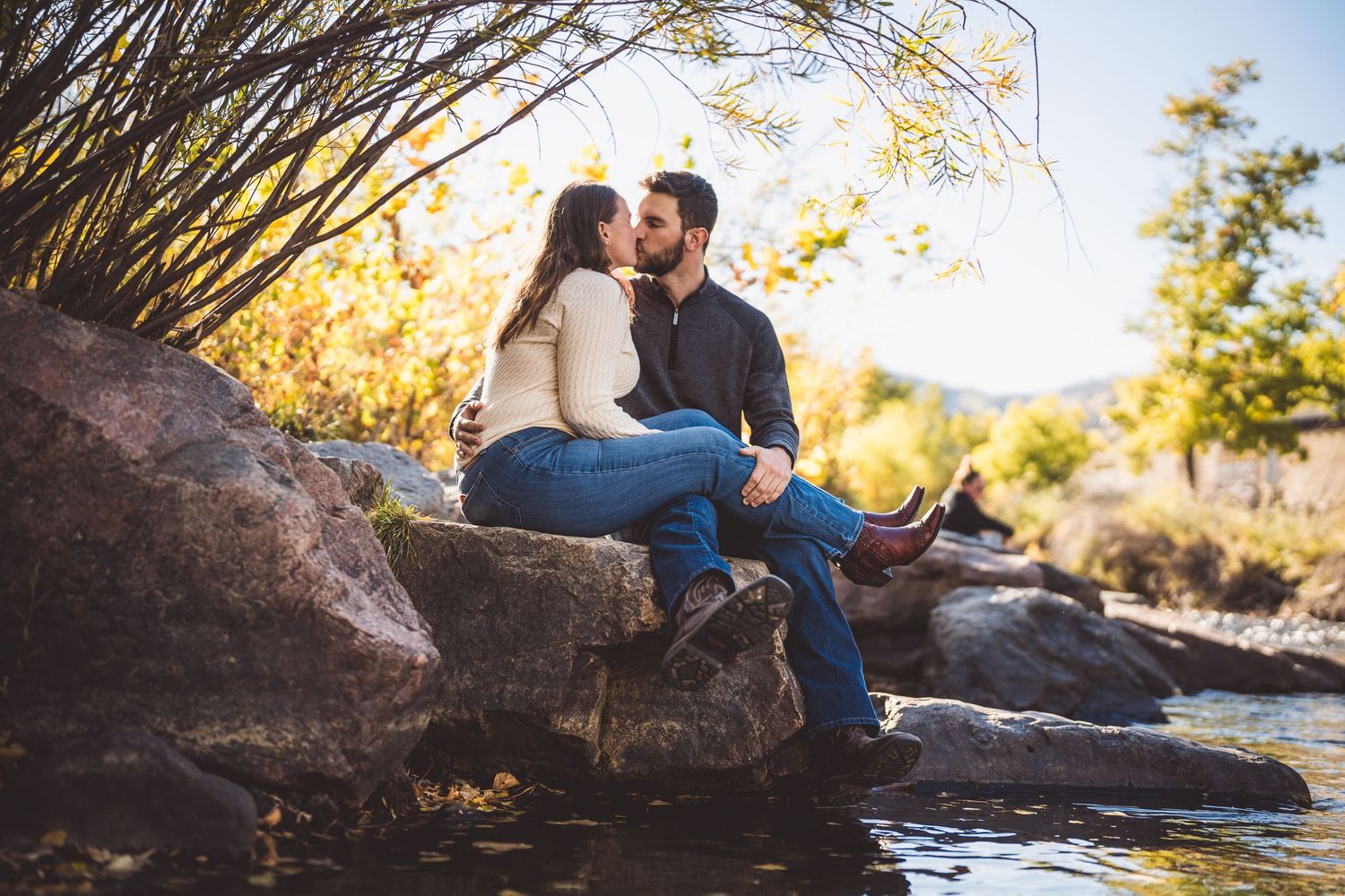 A couple shares an intimate moment by a rocky stream during golden hour in autumn.