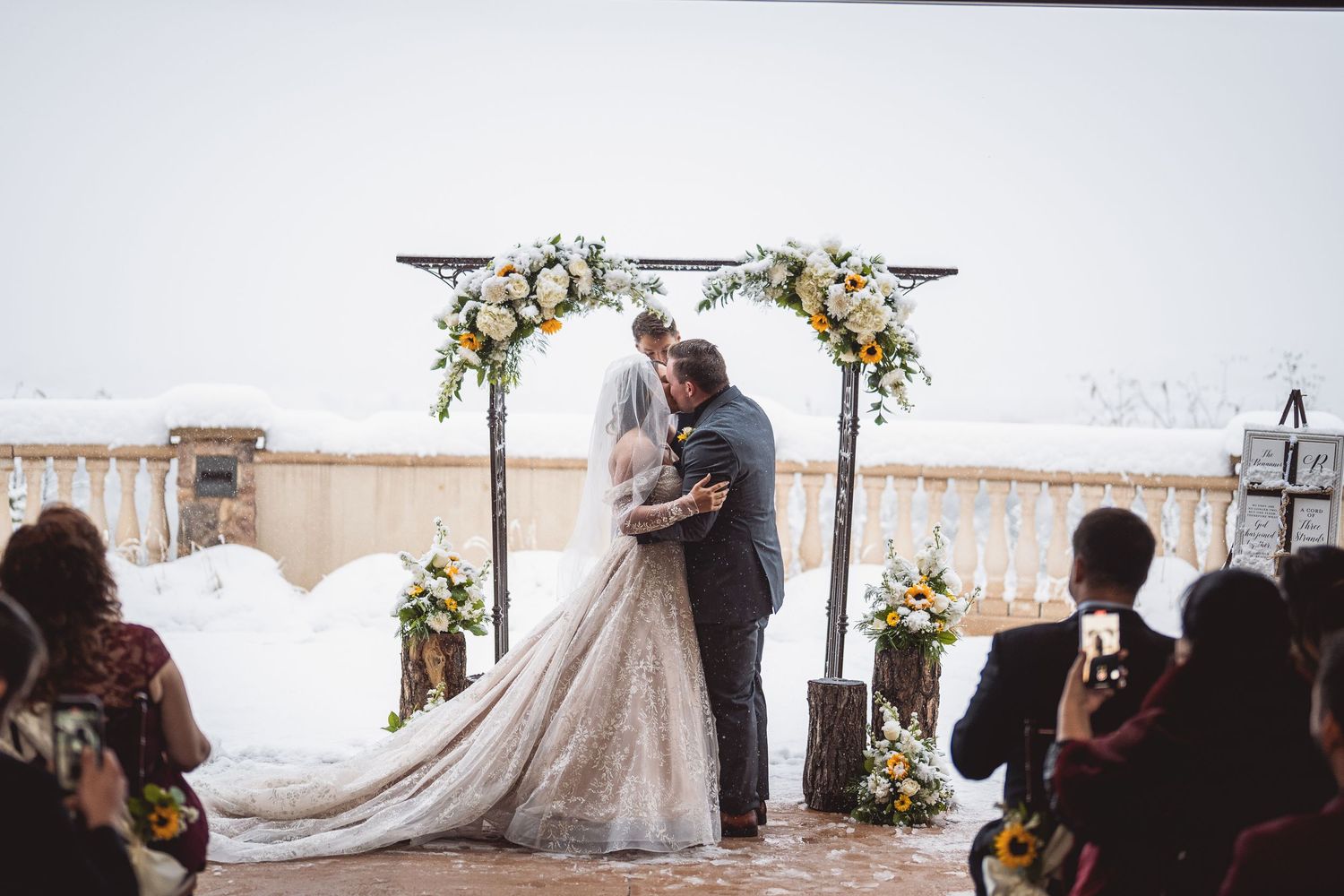 Wedding ceremony in progress with white floral arch and seated guests.