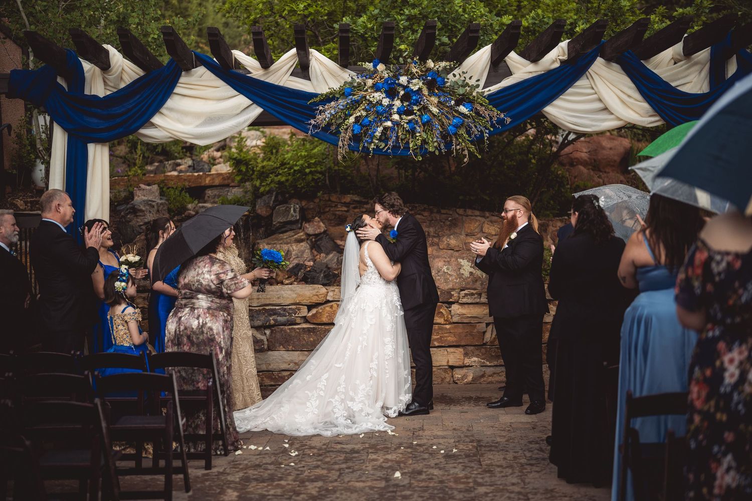 Wedding guests watching a ceremony under a decorated arch with blue accents.