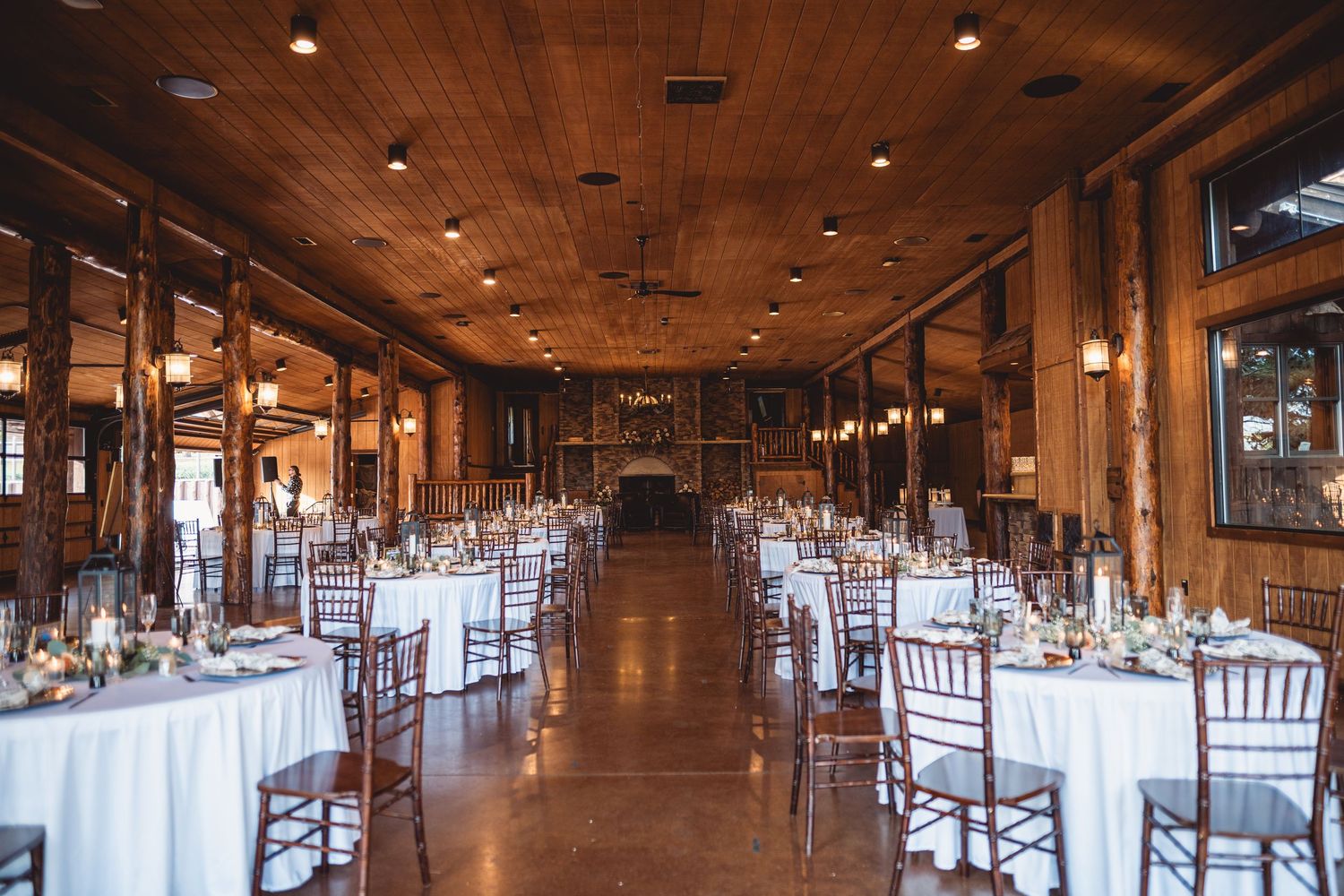 Rustic wooden reception hall decorated with string lights and wooden chairs for an elegant wedding celebration.