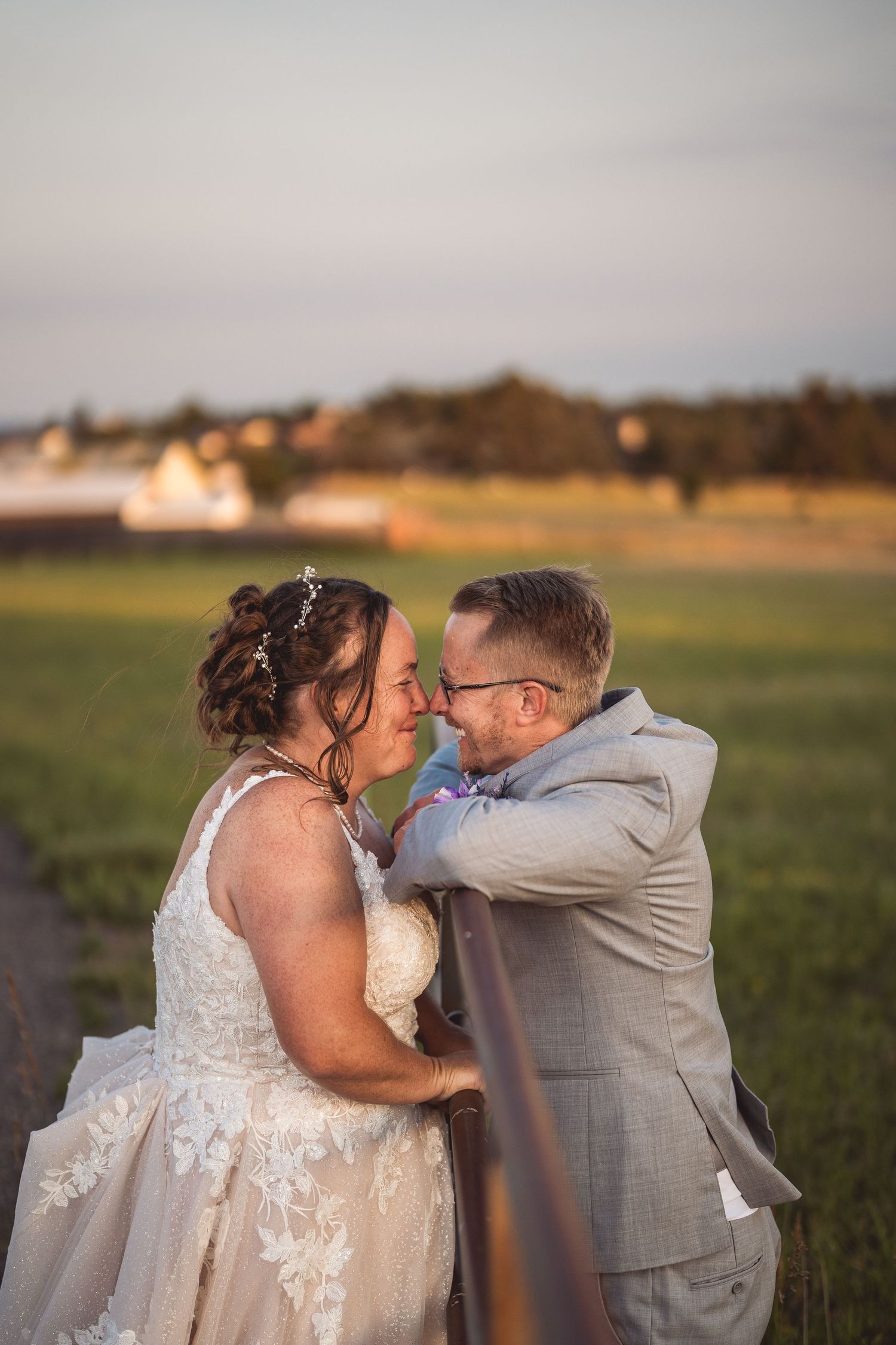 Romantic outdoor wedding moment with couple in white dress and grey suit at sunset.