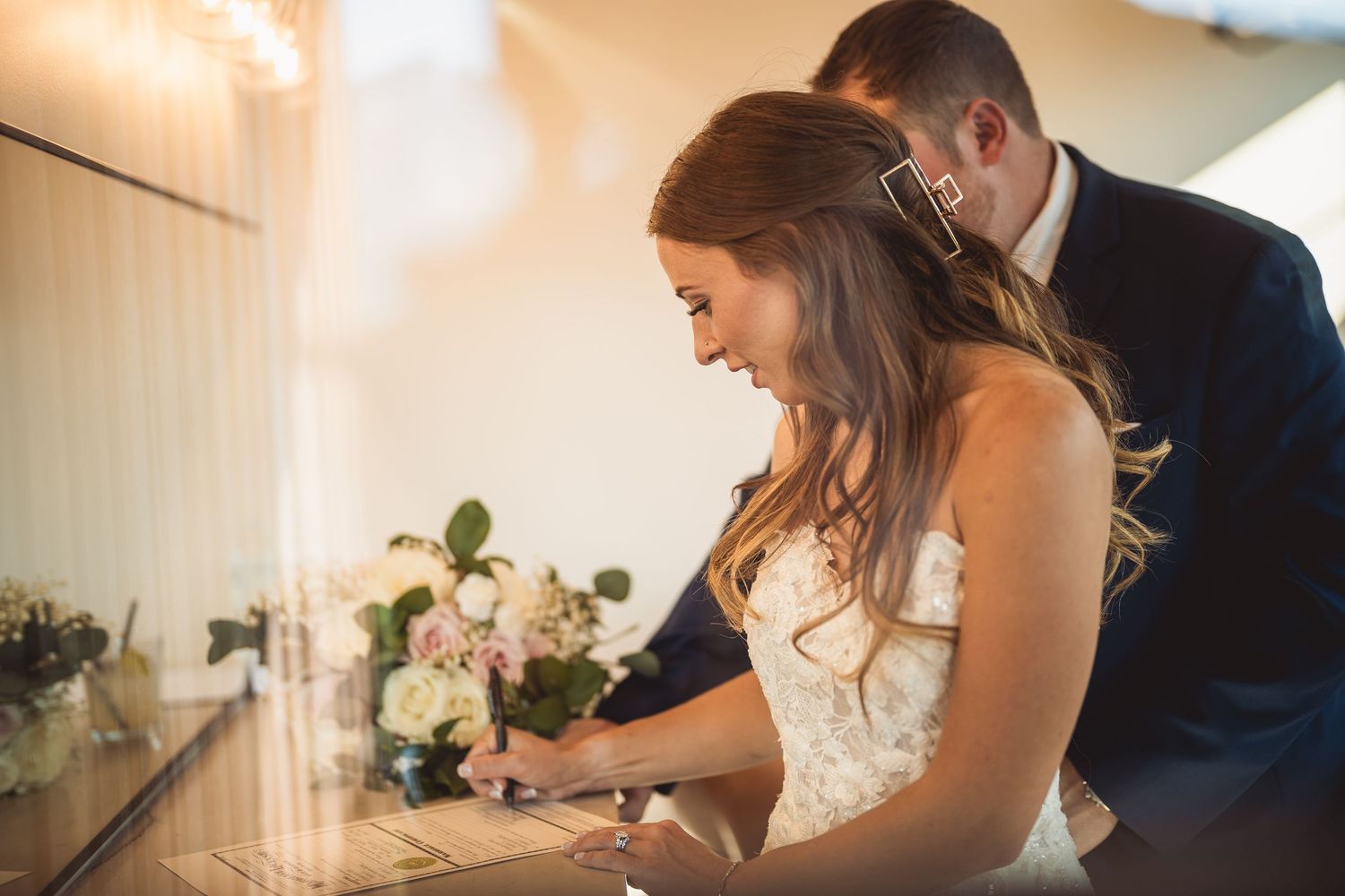 Wedding couple signing documents together at indoor reception venue.