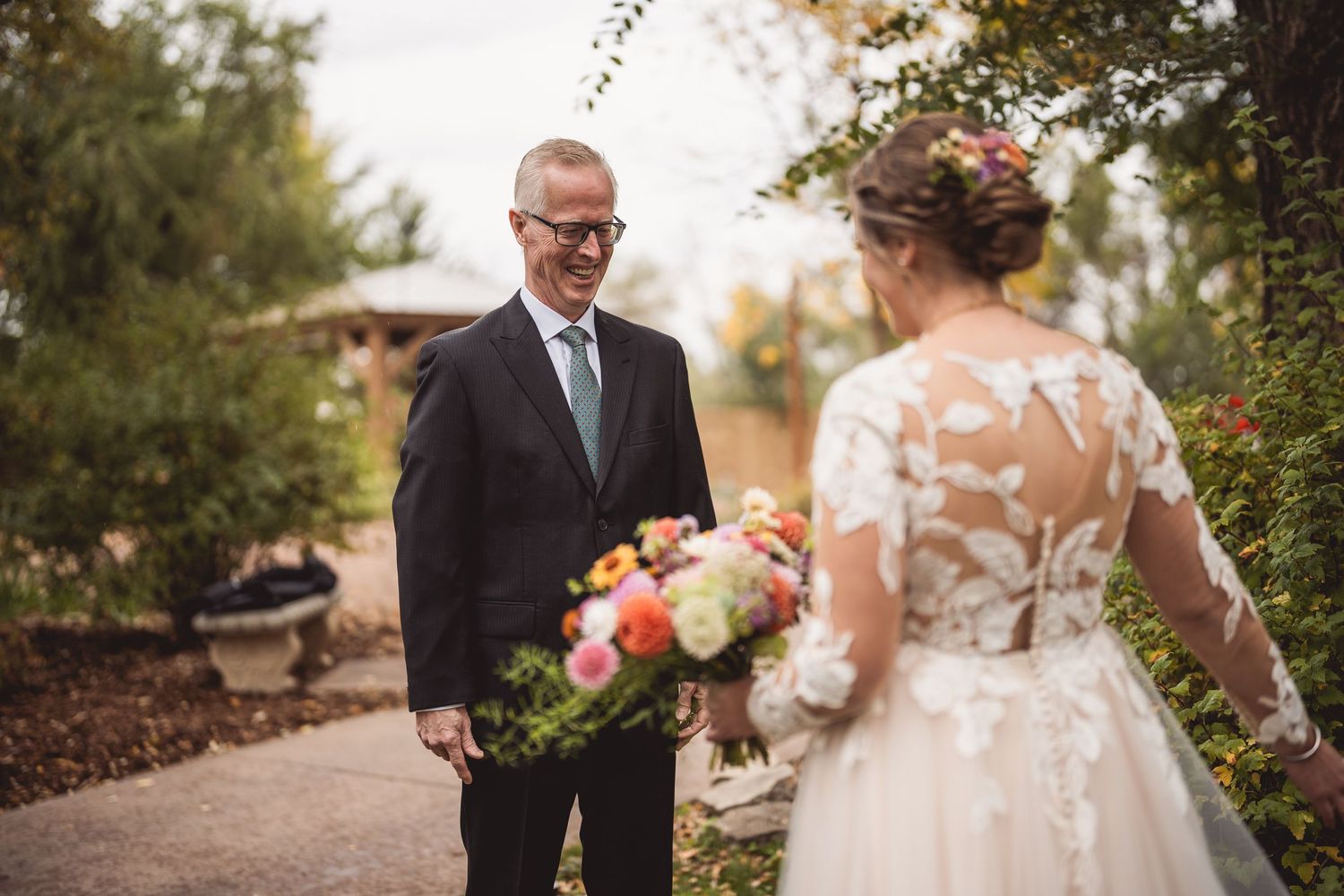 Wedding party members pose on a garden path with decorative lighting and autumn foliage.