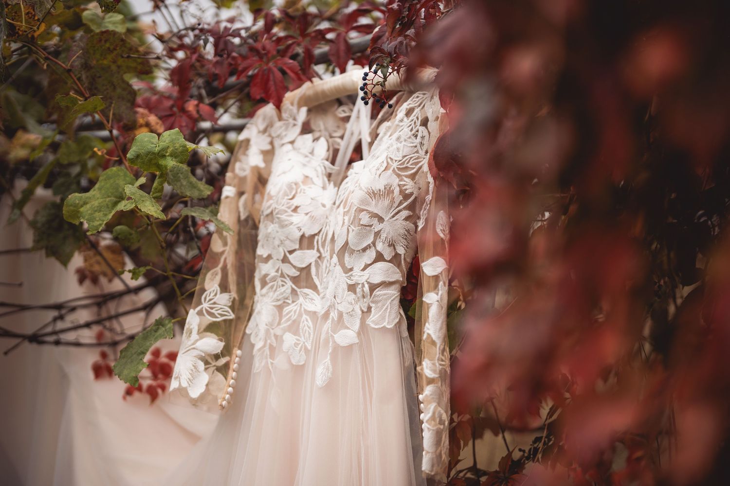 Close-up detail shot of delicate lace wedding dress with burgundy autumn foliage.