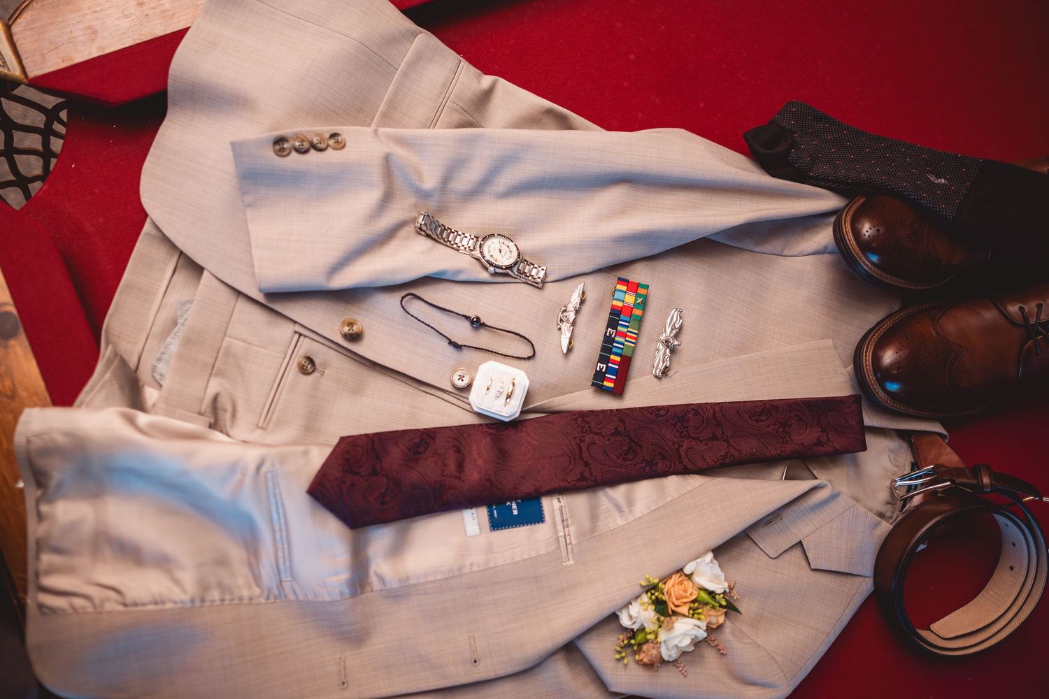 Wedding accessories including suit jacket buttons and festive pins on red velvet.