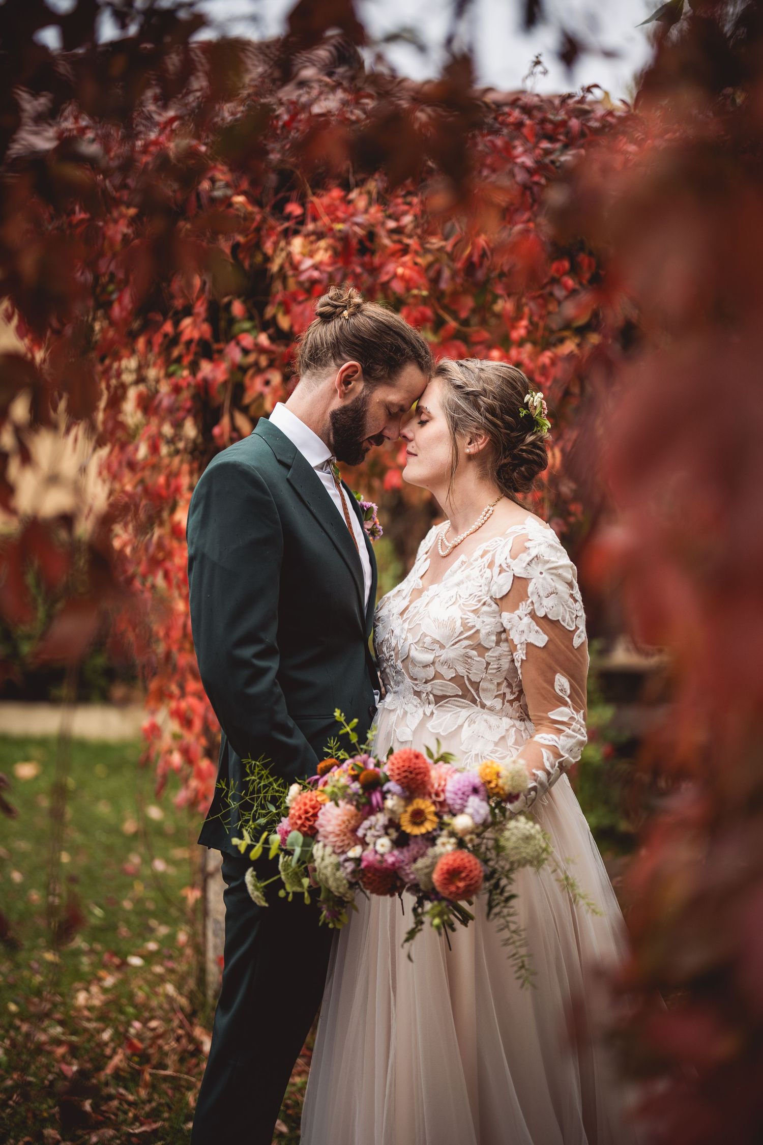 Intimate wedding moment captured under crimson autumn leaves with elegant floral arrangement.