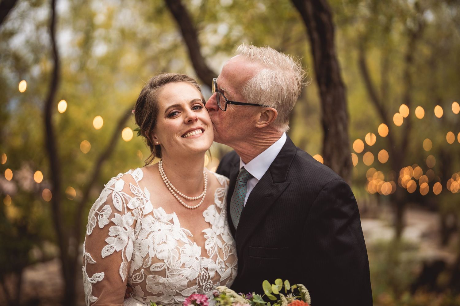 Romantic portrait of couple embracing outdoors with string lights glowing in background.