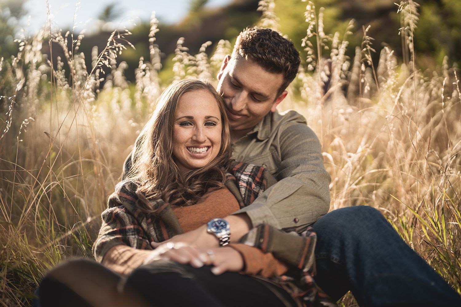 Happy couple relaxes in a sunlit meadow with golden grasses and natural scenery.