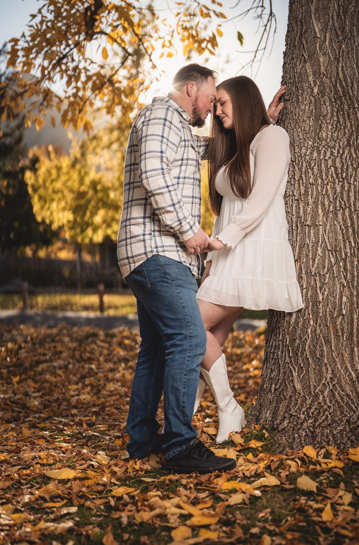 A romantic autumn scene with a couple standing close together under a large tree with golden leaves.