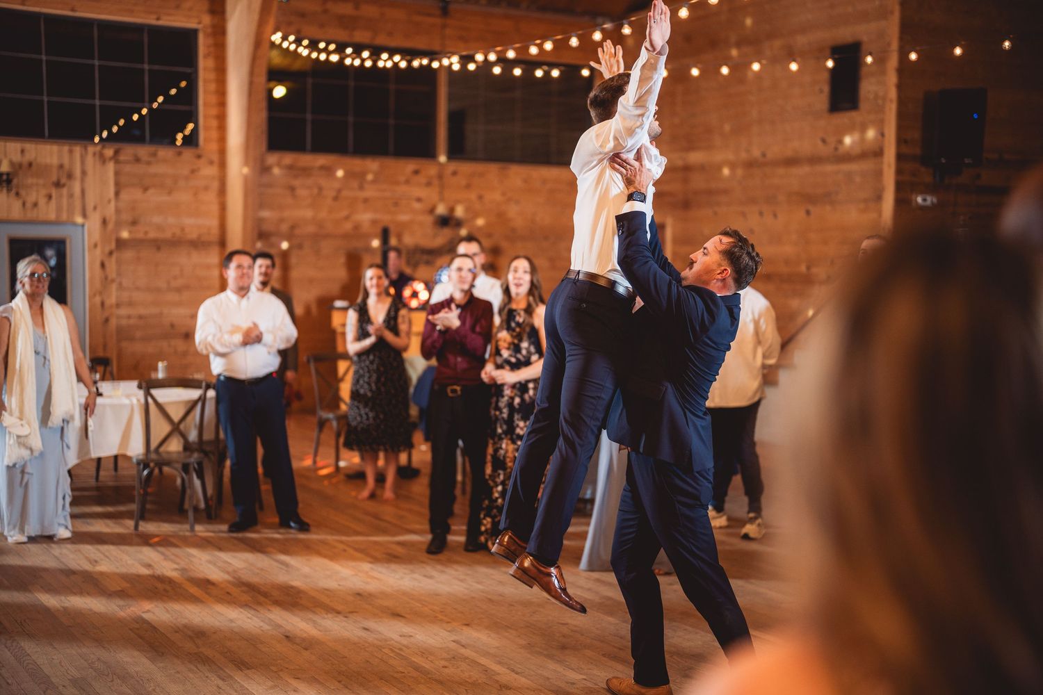 Wedding reception dance floor under warm string lights in rustic indoor venue.