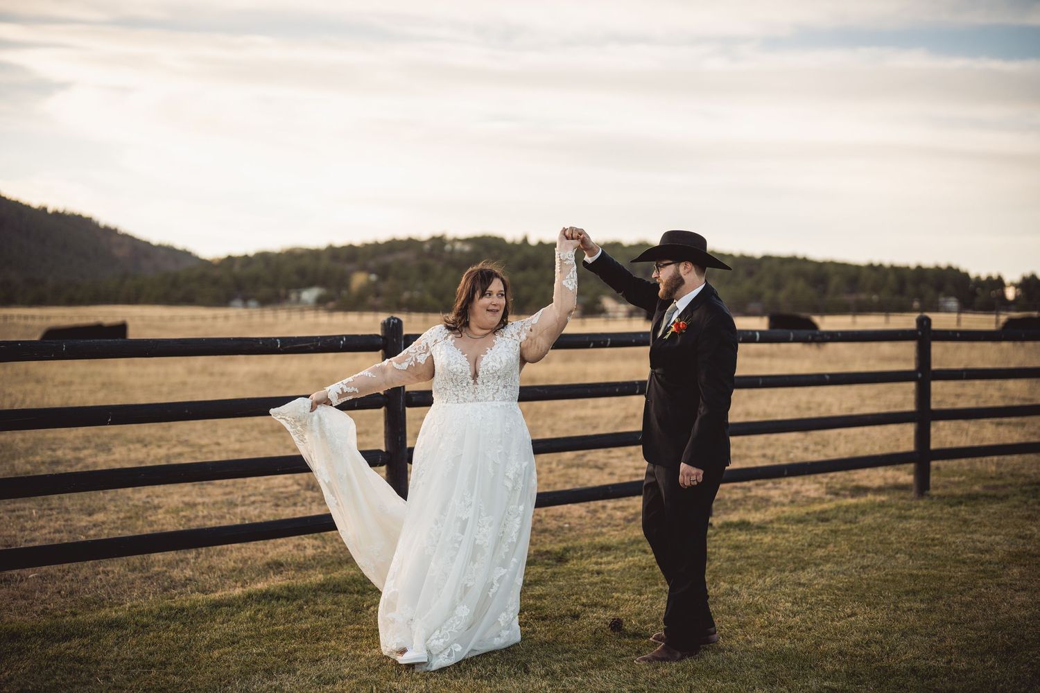 Wedding couple shares romantic moment by wooden fence in countryside setting at sunset.