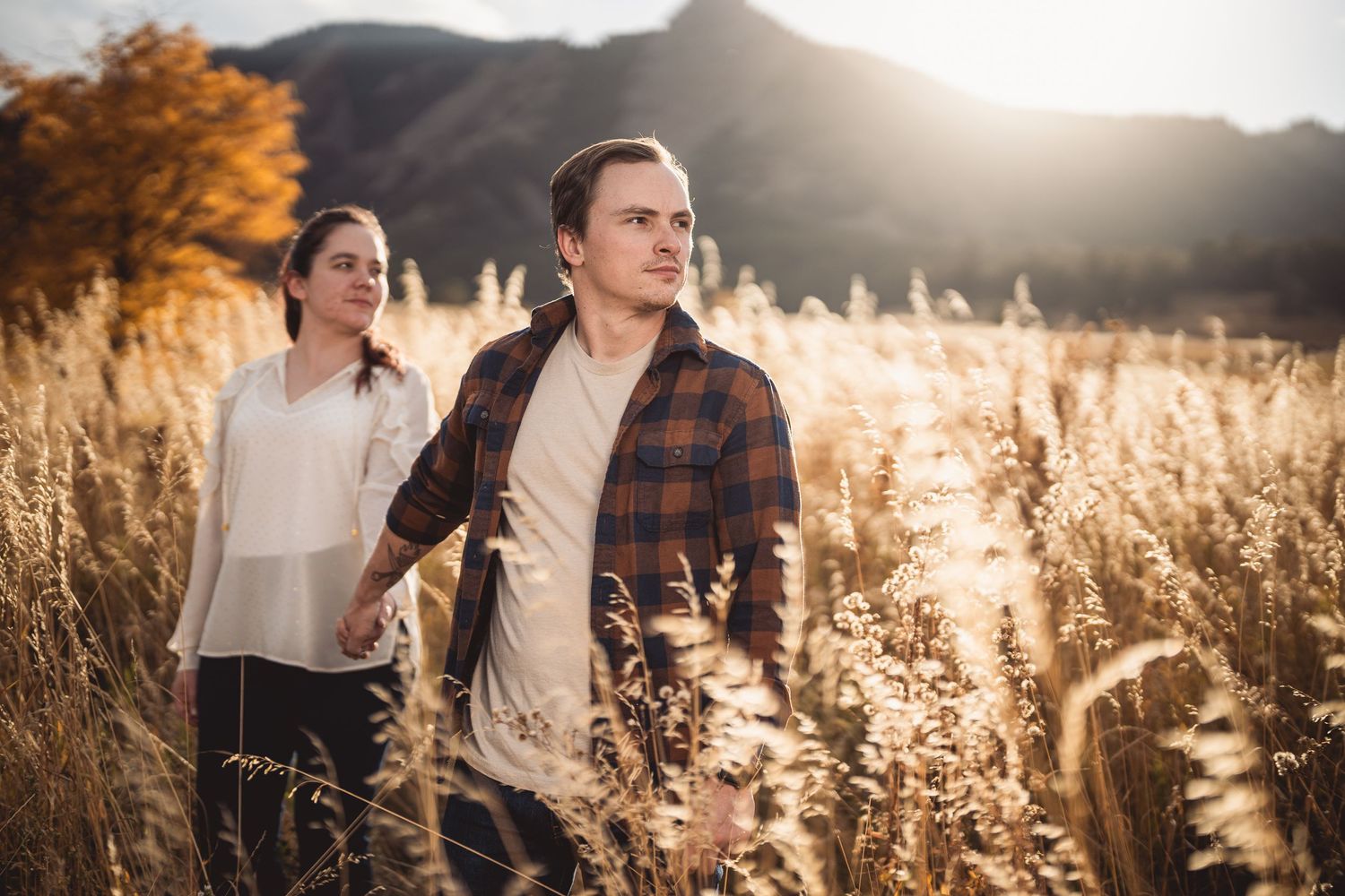 A couple walking through a golden field of tall grass during sunset.