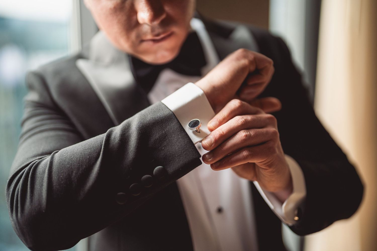 Close-up shot of hands adjusting silver cufflinks on formal shirt sleeve.