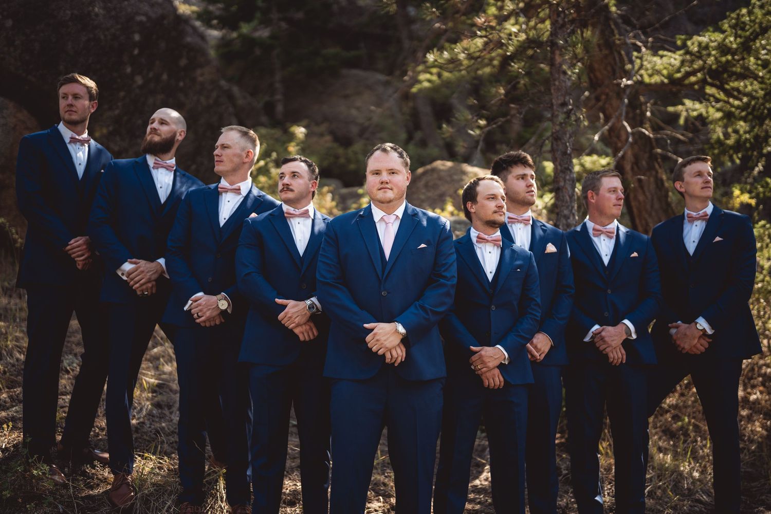 Wedding party members in navy suits pose together on a mountain trail.