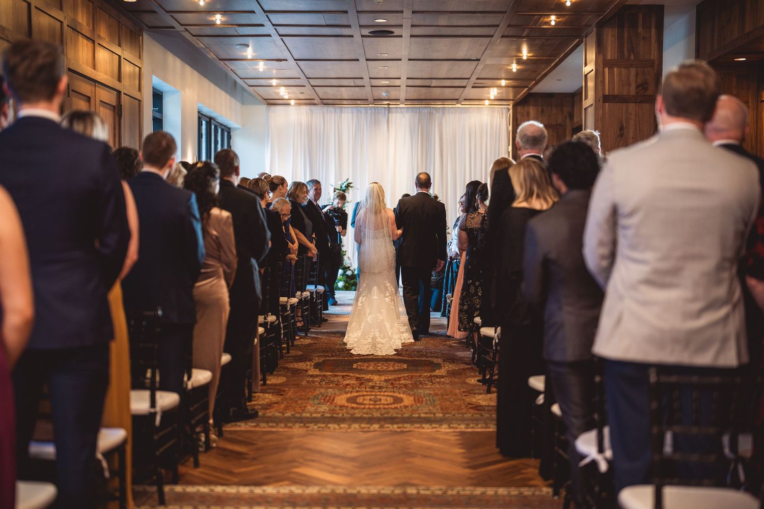 Guests seated in rows at an indoor wedding ceremony with industrial-style ceiling and lighting.
