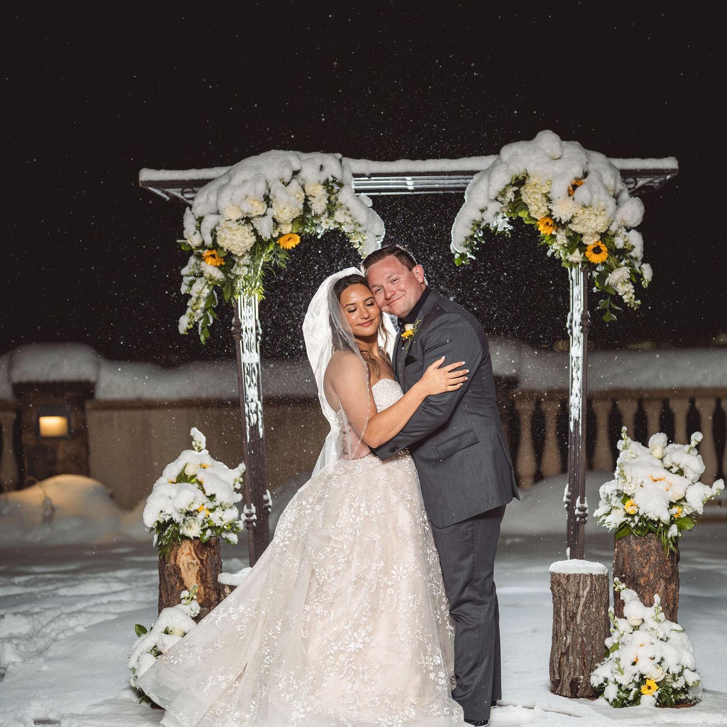 A winter wedding ceremony setup with a white arbor decorated with floral arrangements in the snow.