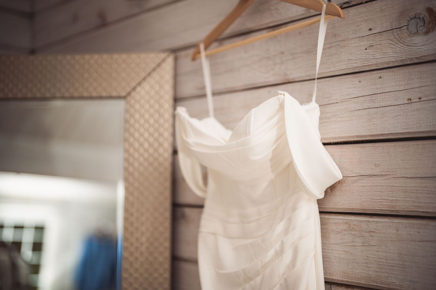 White wedding dress hanging on wooden wall with soft natural lighting.
