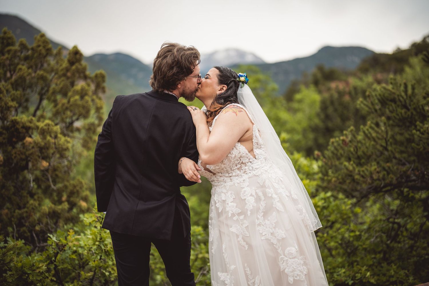 Newlyweds pose for intimate photos against a scenic mountain landscape with flowing wedding dress details.