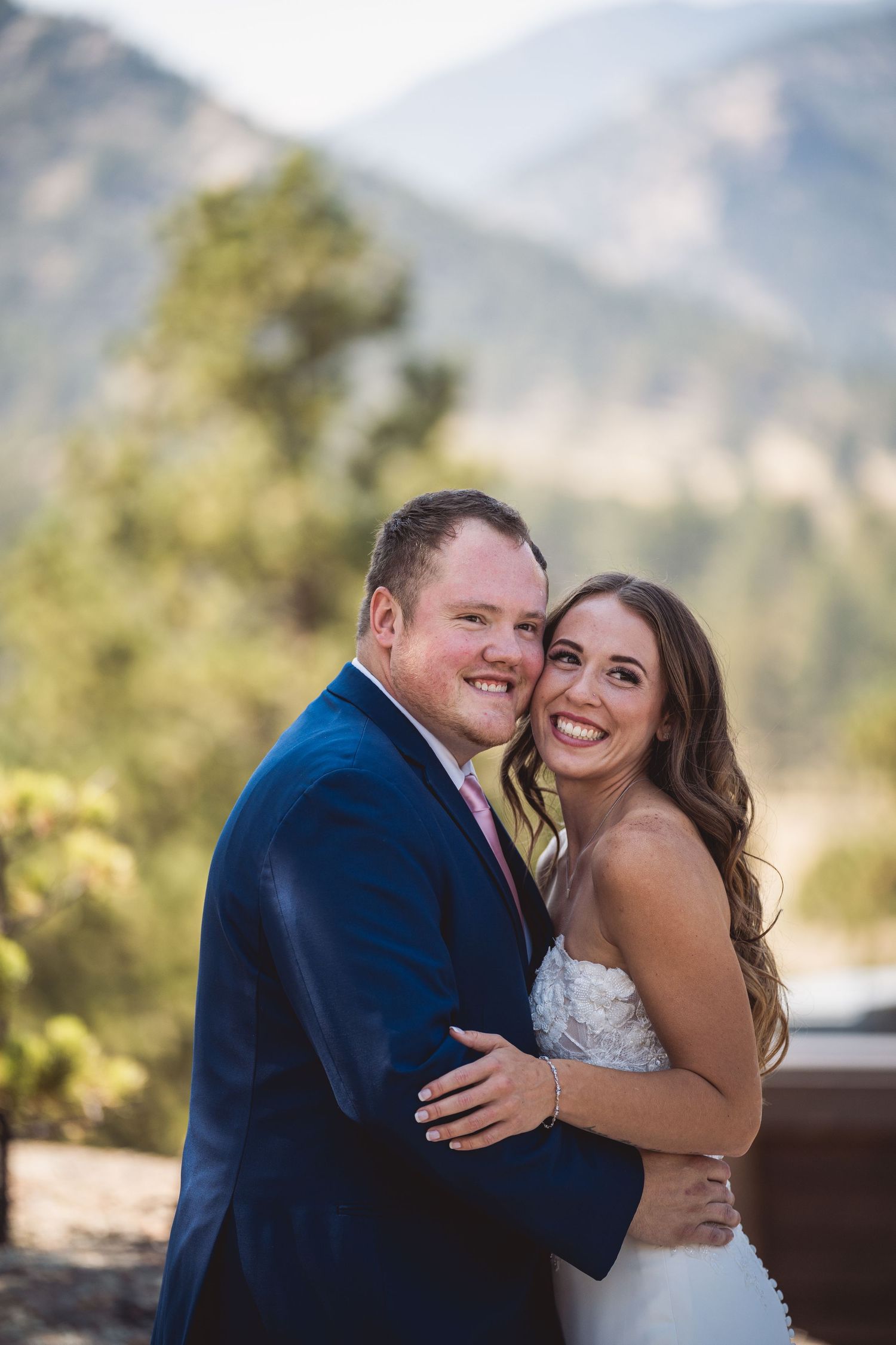 Wedding couple embraces and laughs against a mountain backdrop.