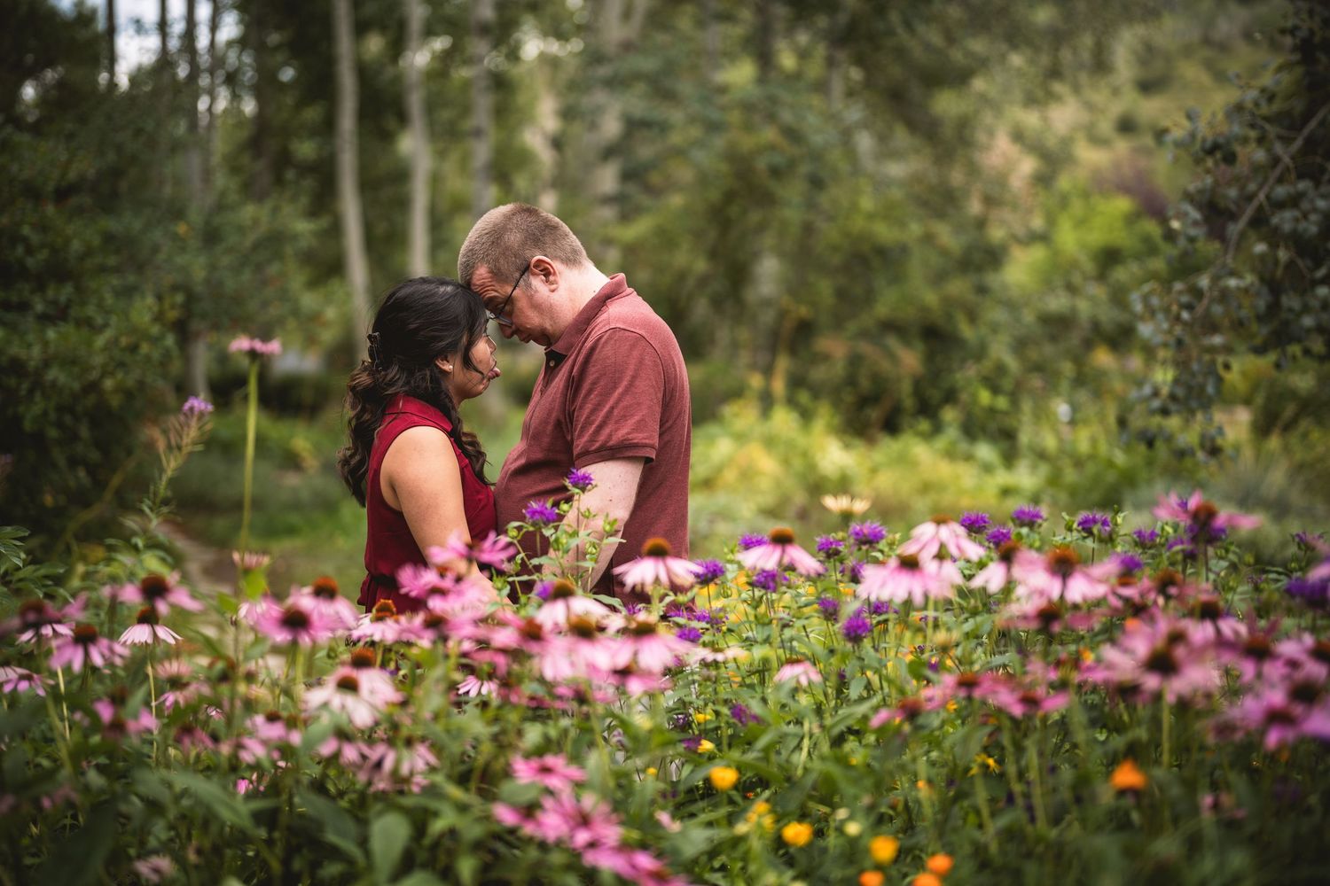 A couple shares an intimate moment among vibrant pink and yellow wildflowers in a garden.