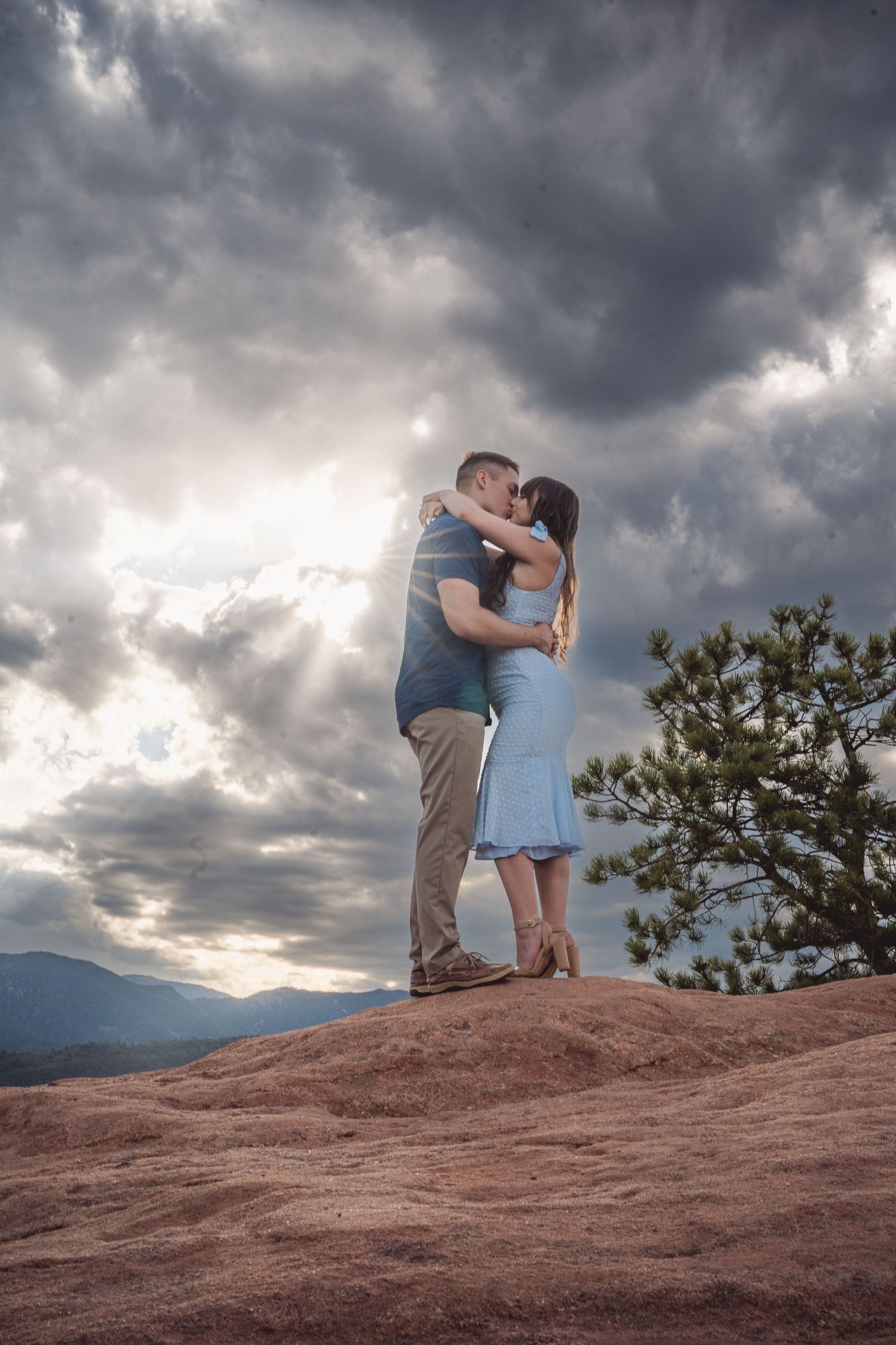 A dramatic sunset embrace on red rocks with storm clouds and mountains in the background.