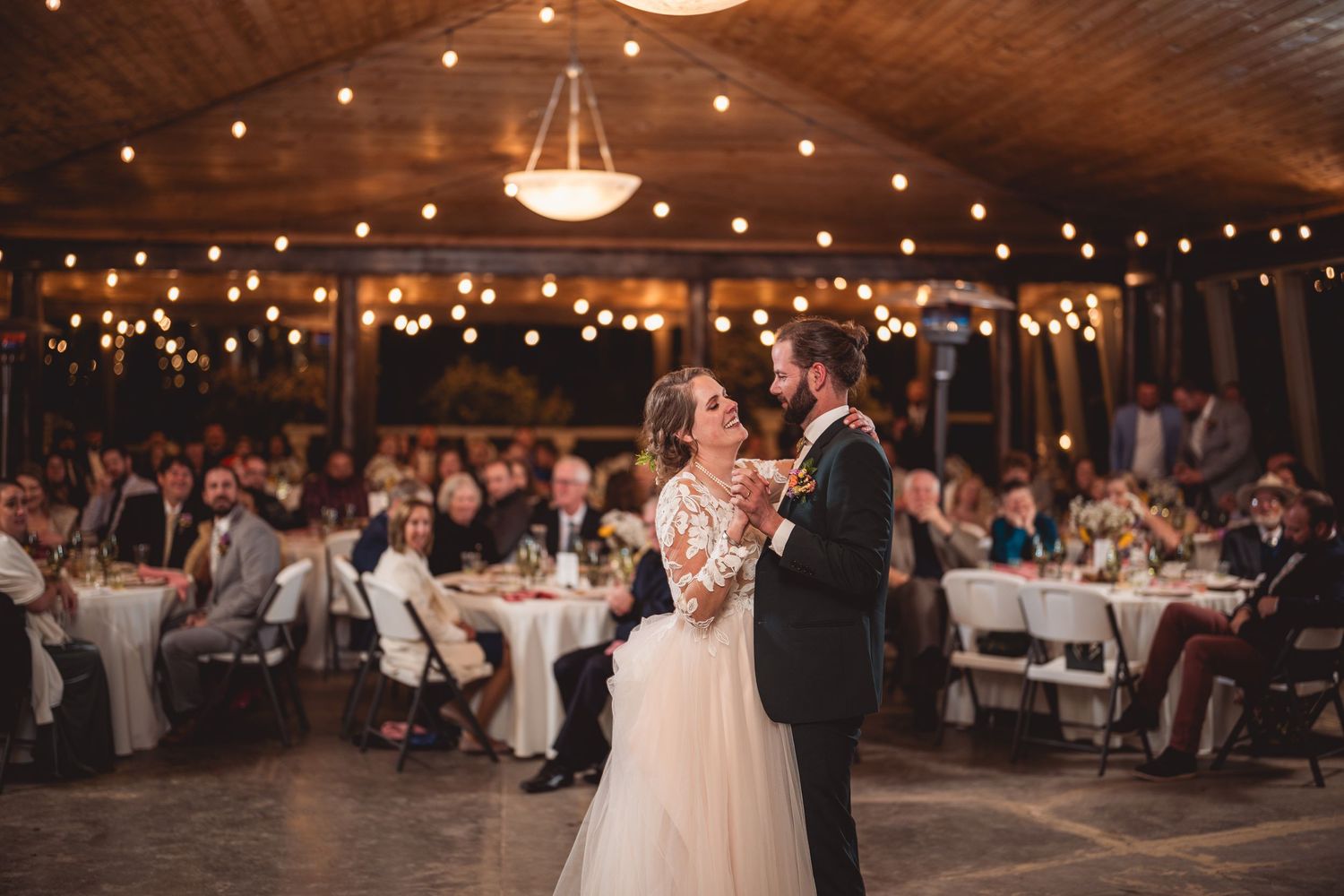 Couple shares an intimate dance moment at their reception under twinkling lights.