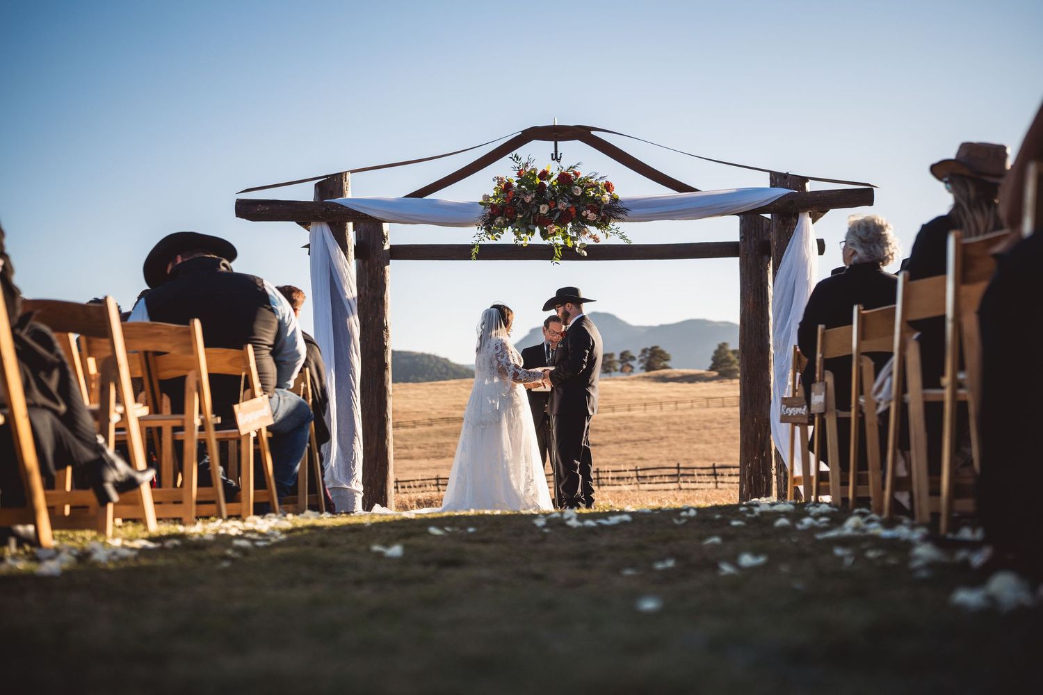Wide-angle shot of outdoor wedding ceremony setup with mountain backdrop and wooden chairs.