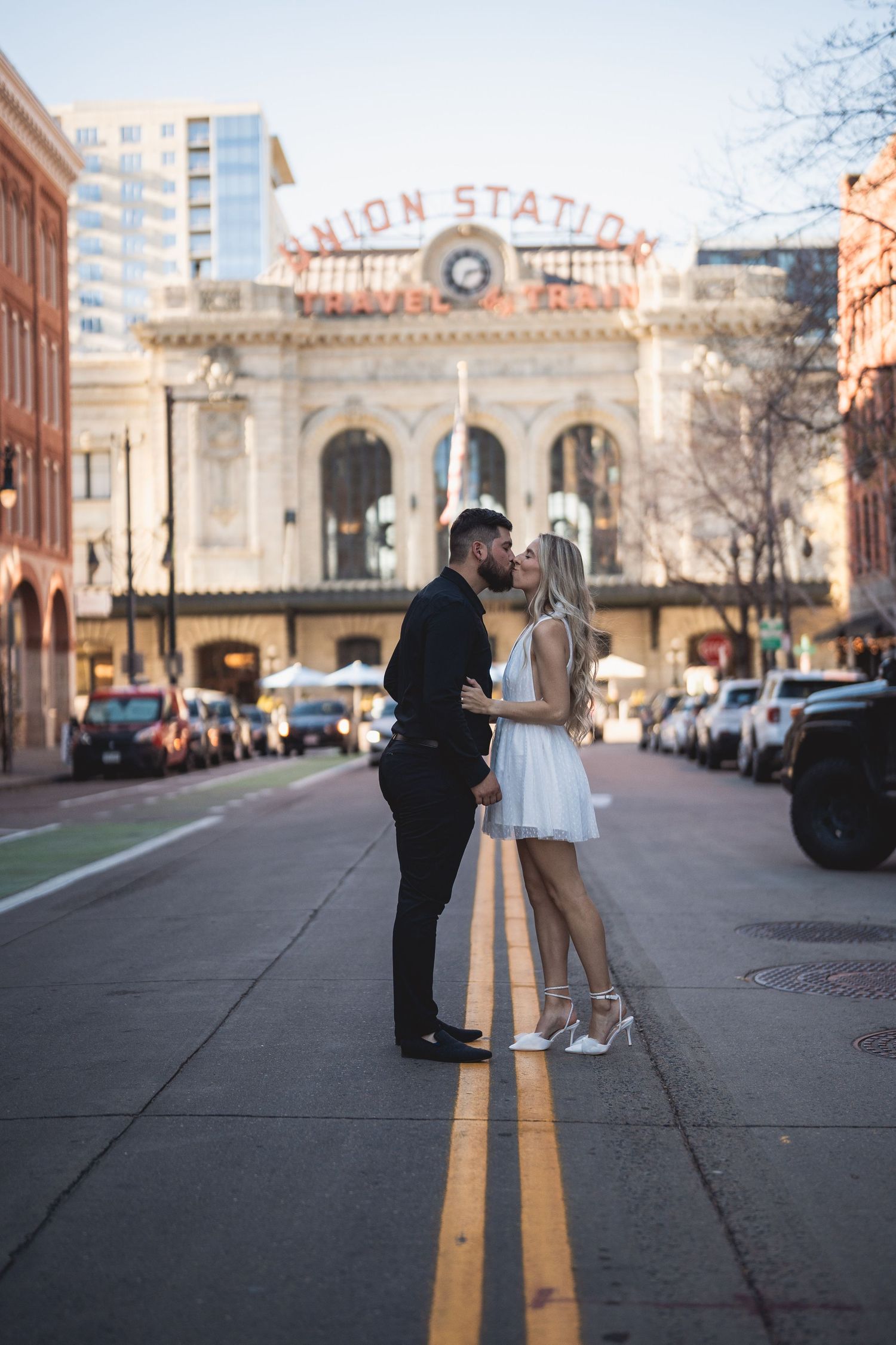 Couple sharing a romantic kiss on the street in front of Denver Union Station in wedding attire.