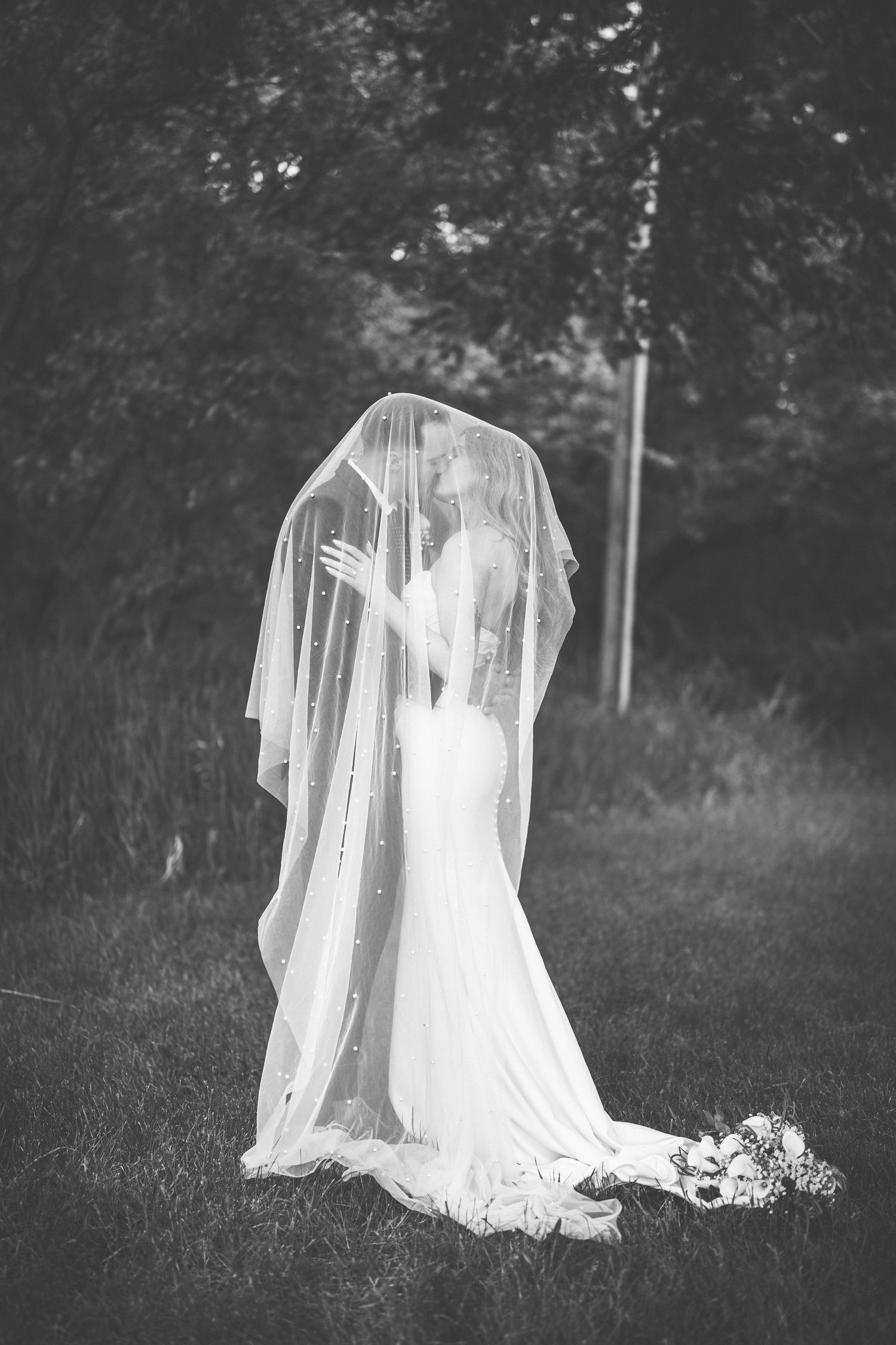 Black and white portrait of flowing wedding dress and veil in grassy field.