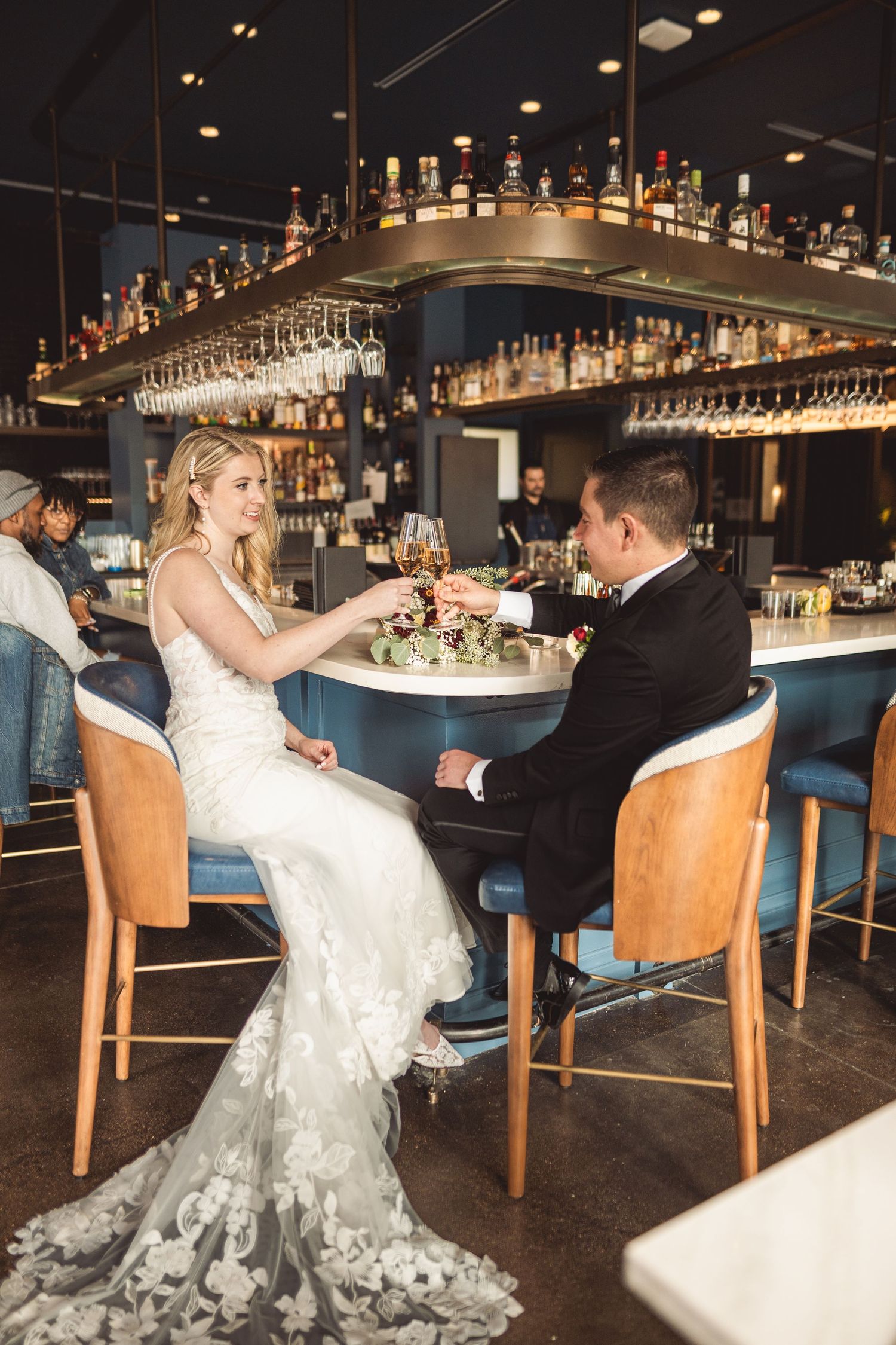 Wedding couple poses at an upscale bar with leather chairs and ambient lighting.