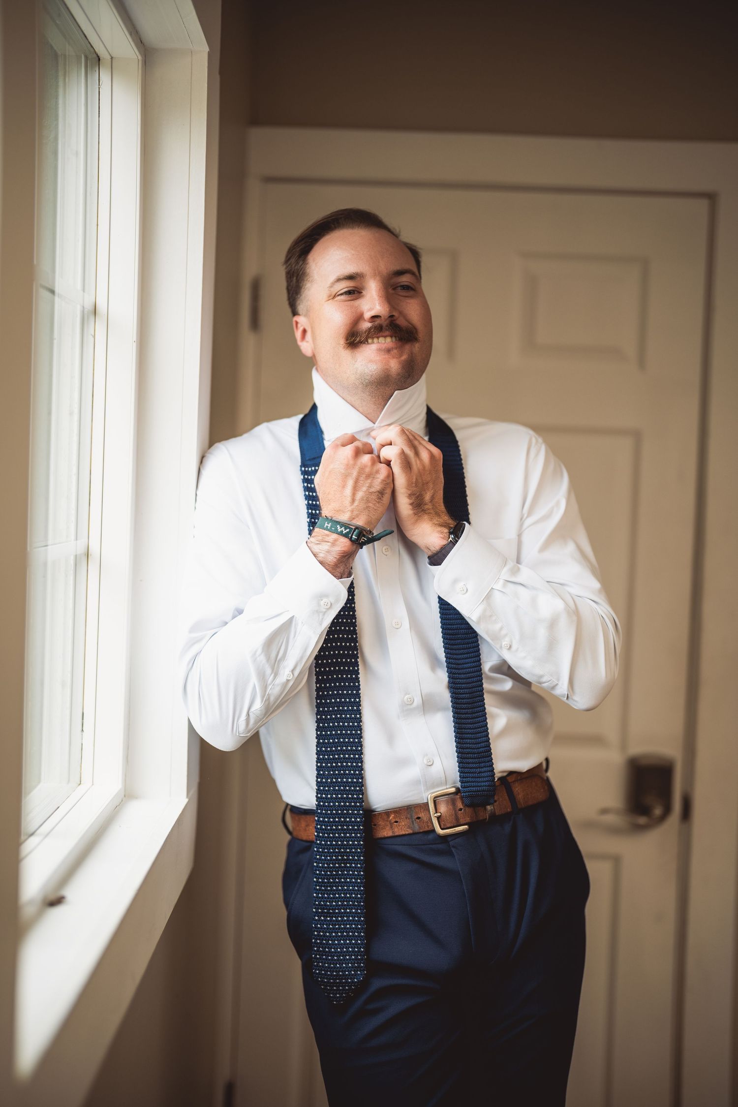 Person in navy suit with suspenders and tie adjusts formal attire.