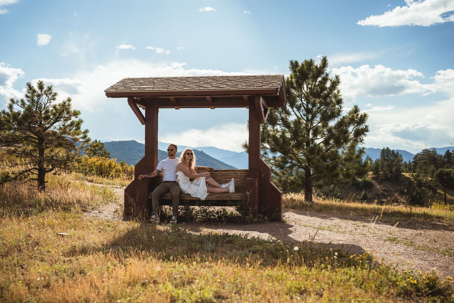 Couple relaxing at wooden shelter with mountain landscape views.