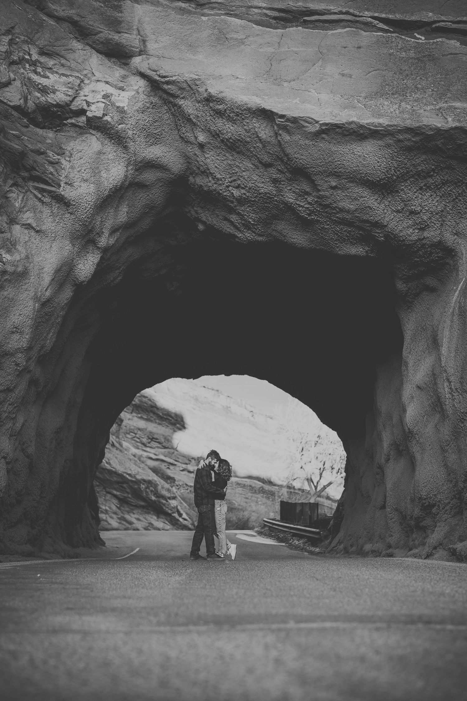 Two silhouettes share a moment in front of a natural rock arch formation.