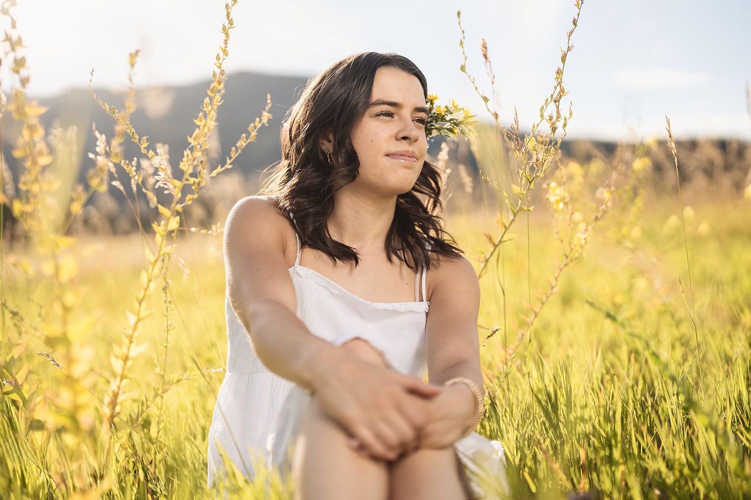 Young woman in white dress sitting in golden sunlit field smiling peacefully outdoors.