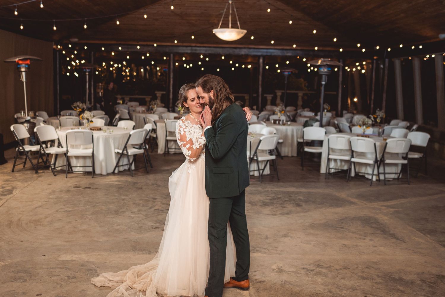 Reception hall decorated with string lights and macrame backdrop for wedding ceremony.
