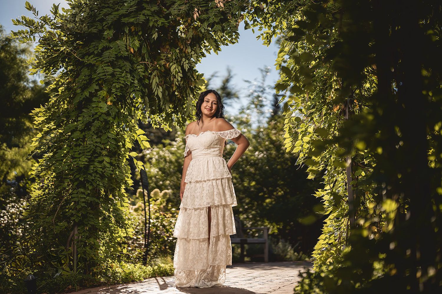 Ethereal outdoor portrait featuring a layered white dress in a garden setting with dappled sunlight.