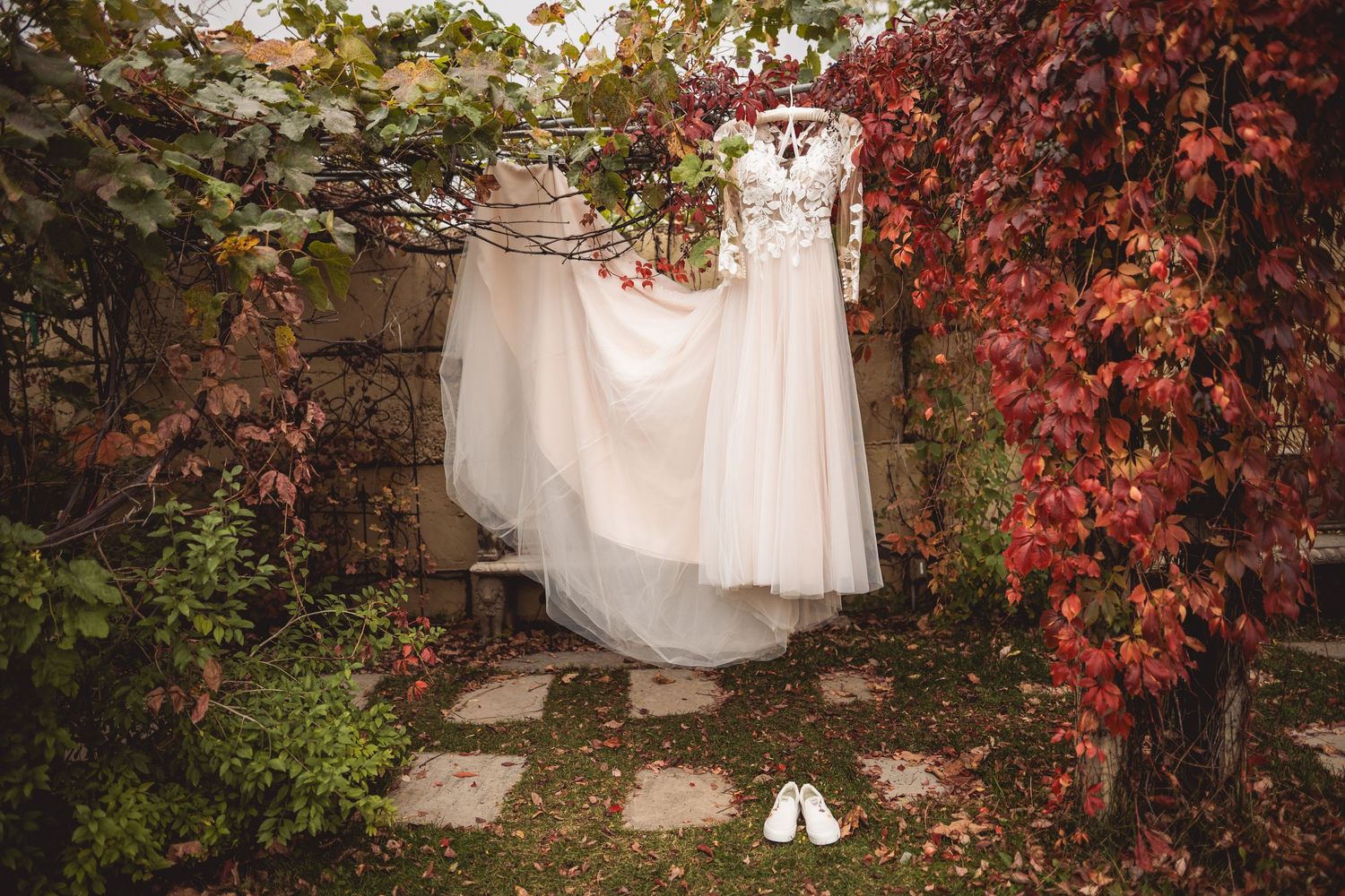 Wedding dress and shoes displayed against a wall with red ivy leaves.