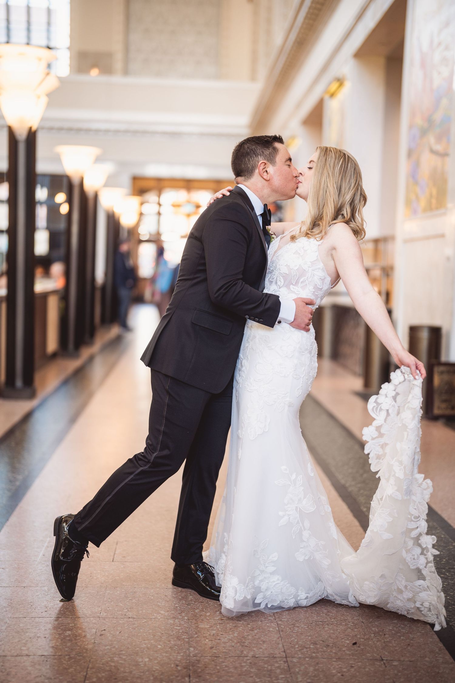 Romantic wedding couple dips and kisses in an elegant hallway with white dress and black suit.