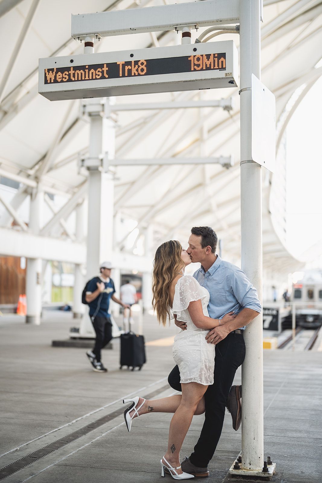 Couple shares romantic moment in bright white covered walkway with transit signage.