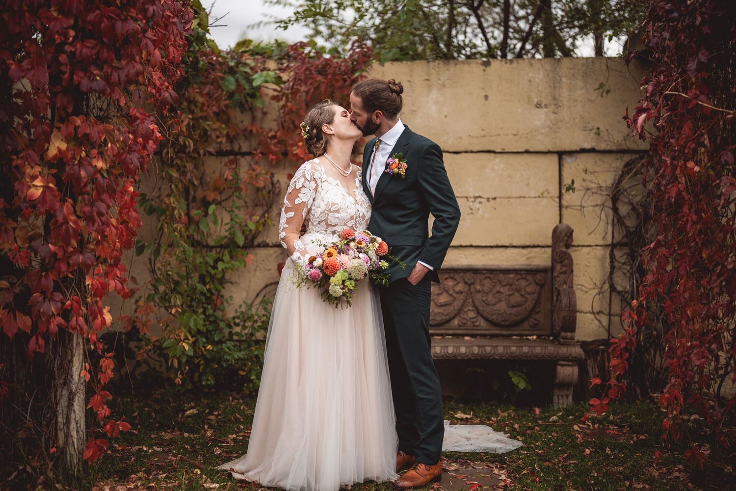 Intimate wedding moment captured against backdrop of red autumn leaves.