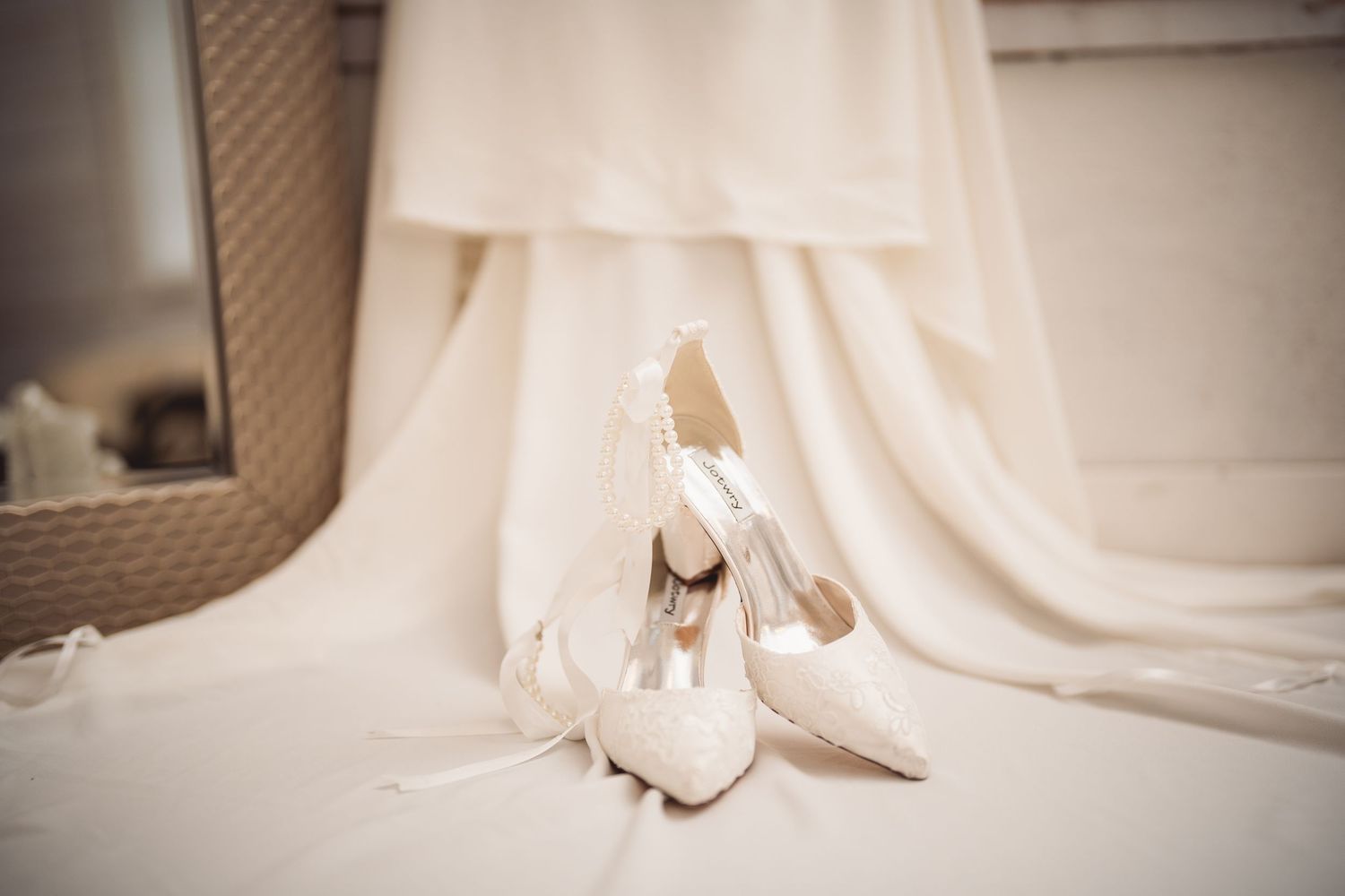 Close-up details of white wedding dress train and fabric on wooden floor.